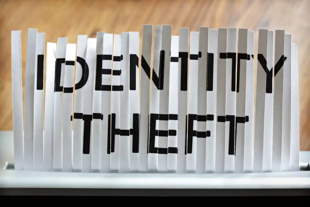 A piece of paper with the words IDENTITY THEFT is partially shredded in a paper shredder, symbolizing the destruction or protection of personal information.